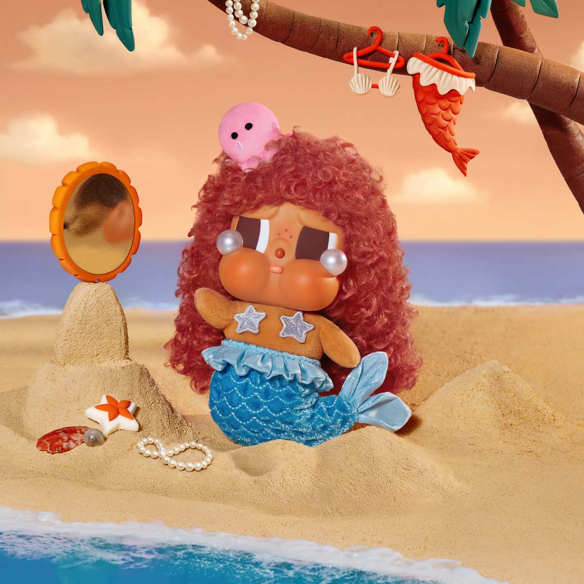Mermaid toy with red hair and blue tail on a sandy beach with ocean view - little c land