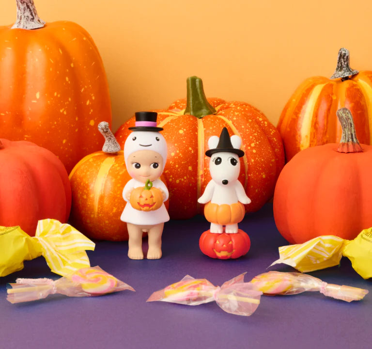 Halloween-themed figurines and pumpkins with candy on a purple surface against an orange background