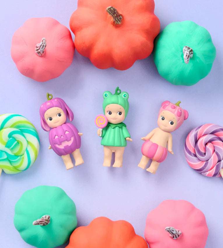 Colorful toy figures with pumpkins and lollipops on a light purple background