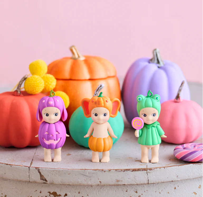 Three colorful figurines in front of pastel pumpkins on a wooden surface.